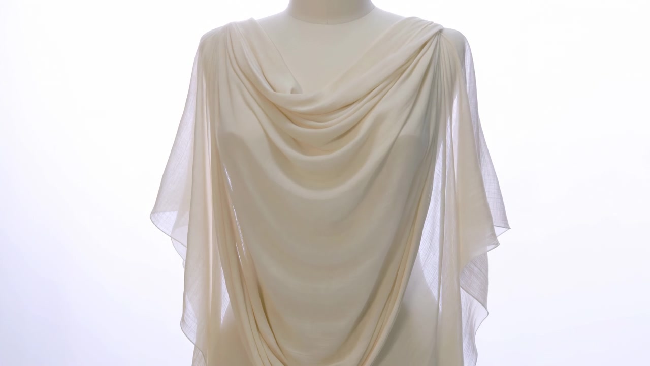 Mannequin torso wrapped in lightweight beige fabric shaped into deep layered folds at chest, with translucent side panels and soft settling movement under bright white studio backlight