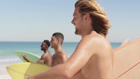 hombres jóvenes en la playa llevando tablas de surf 4k