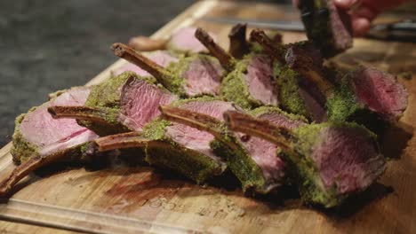 chef lays out venison meat ribs slices, with green spice on top, on wooden cut board