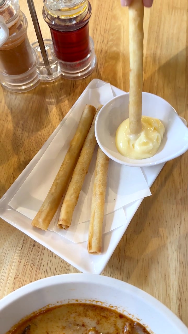 Tangan mengambil lumpia renyah, mencelupkannya ke dalam saus, di bawah pencahayaan restoran yang terang, dari sudut pandang atas.