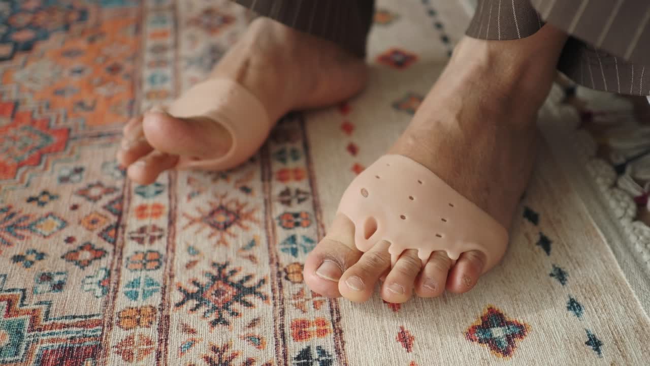 Desenli bir halı üzerinde silikon parmak ayırıcılar takmış bir kişinin ayakları.