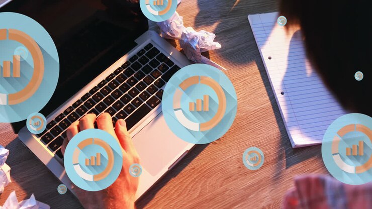 Animation of graph icons, overhead view of biracial man working on laptop and writing in notepad