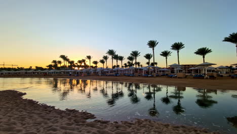 Hora-Dorada-En-Un-Tranquilo-Balneario-Egipcio-Con-Palmeras-Y-Aguas-Tranquilas-Que-Reflejan-El-Cielo-Sereno,-Toma-Amplia