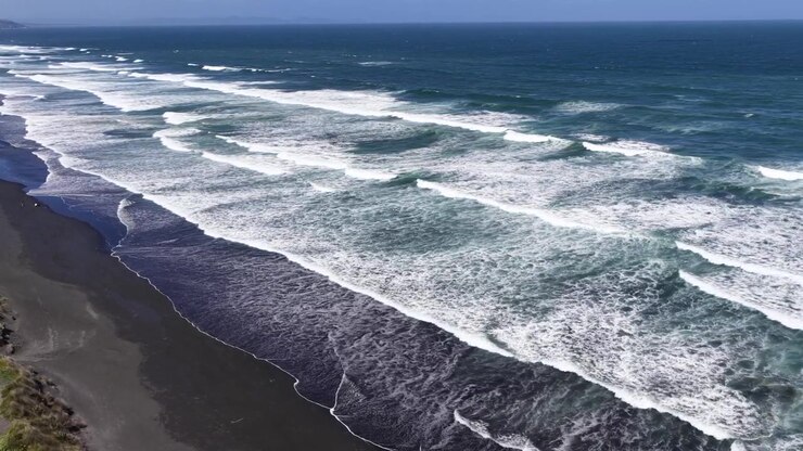 Ripresa aerea con drone di onde potenti che si infrangono sulla costa di sabbia nera dell'Isola del Nord della Nuova Zelanda, vista del paesaggio costiero.