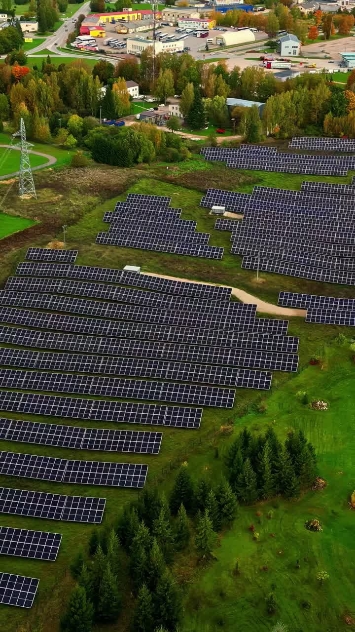 Aerial view of large solar power plant beside commercial district and forest, vertical