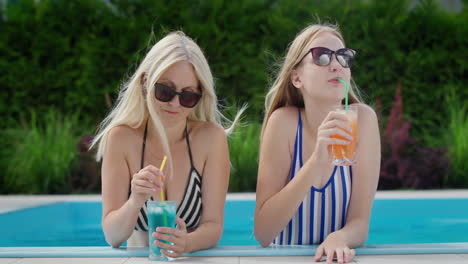 mom and teenage daughter relax by the pool, drinking cocktails