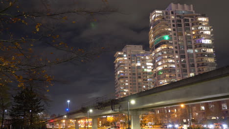 Trains-Running-On-The-Railway-Over-Busy-Streets-In-Downtown-Vancouver-At-Night---low-angle,-time-lapse