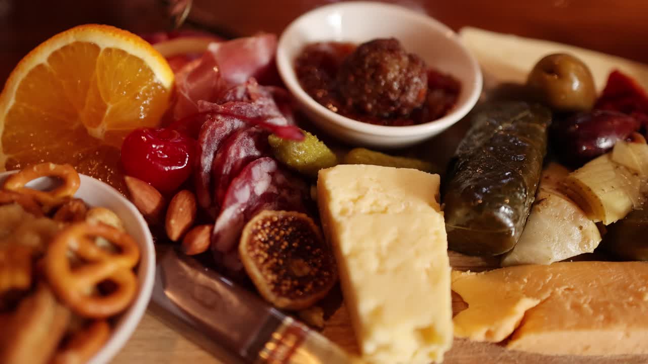Charcuterie board with cheese, crackers, olives, meats, and dips under warm, soft lighting rotates slowly