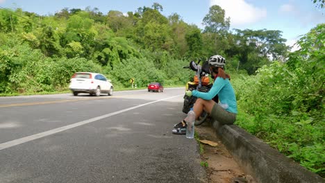 asiático tomando un descanso después de un refrigerio en bicicleta en el arcén de una carretera del sudeste asiático