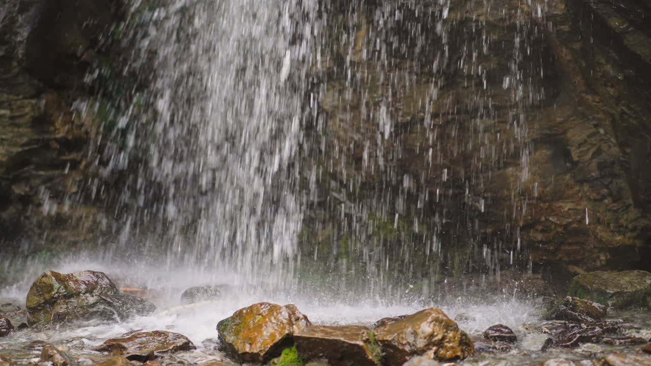 Water jets fall down into pool with stones at wild highland