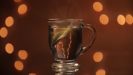 green tea bag being dropped into a steaming glass mug on a beautiful bokeh backdrop