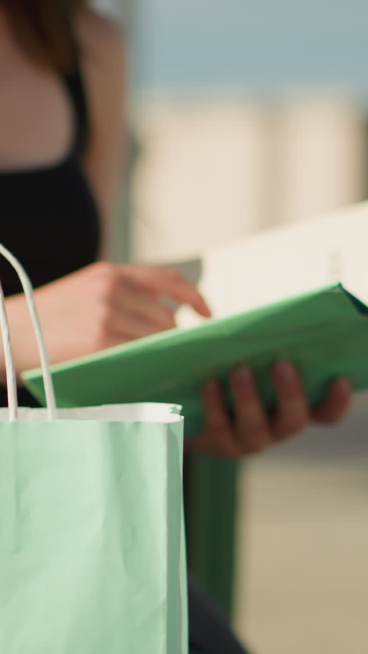 멘트 녹색 쇼핑 가방에서 멘트 색의 책을 가져오는 여자의 클로즈업, 그녀는 페이지를 뒤집고, 그녀의 상체가 배경에서 약간 흐릿합니다.