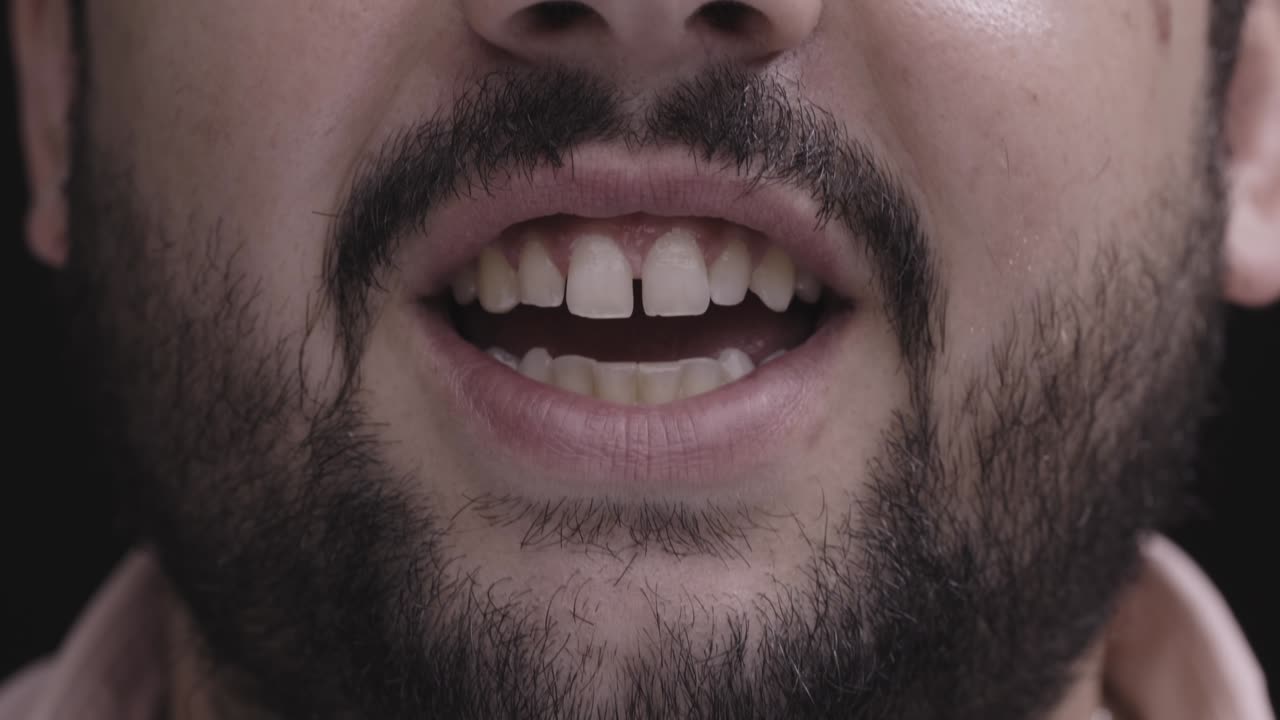 Close up of a man's mouth talking and smiling with slight tooth gap and full beard