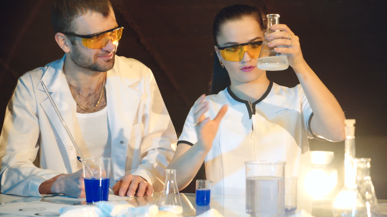 two doctors in eyglasses are experimenting with test tubes with chemicals at a table in the laboratory on a black background