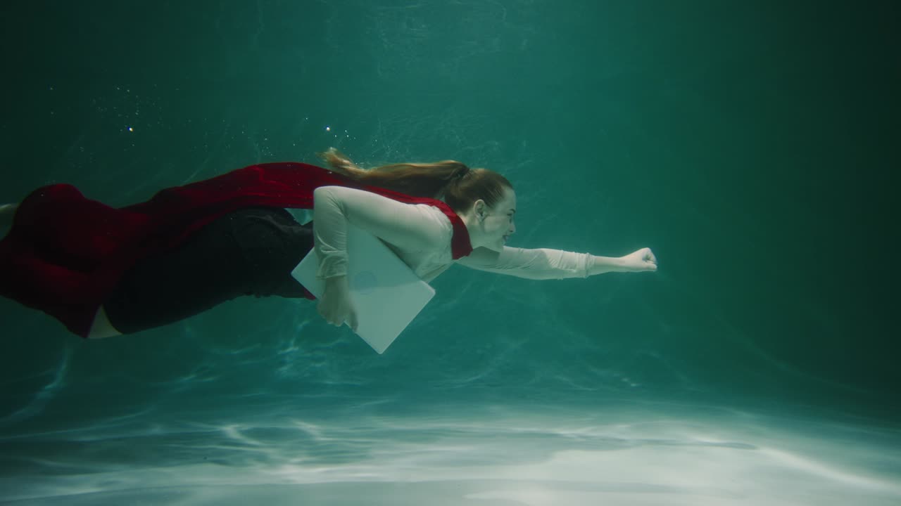 은 슈퍼 히어로 케이프 슈트를 입은 아름다운 젊은 사업가 여성이 노트북 슬로우 모션으로 물 에서 수영합니다.
