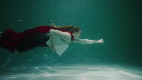 customer service. beautiful young business woman with red superhero cape suit swims underwater with laptop slow motion.