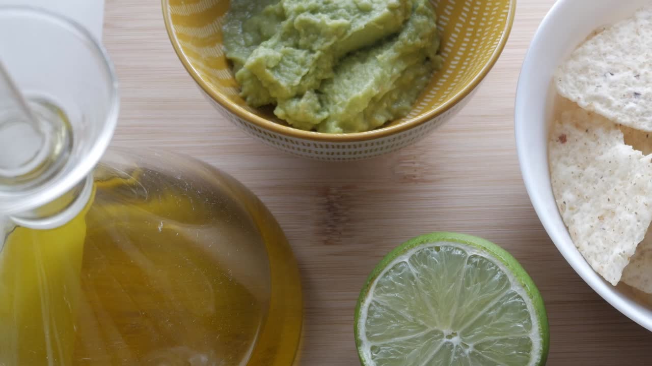 Freshly made guacamole with chips, lime, and olive oil on a wooden surface