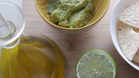 freshly made guacamole with chips, lime, and olive oil on a wooden surface