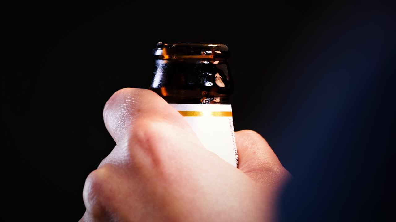 A hand skillfully uses a bottle opener to remove a cap from a beer bottle in a close-up view.
