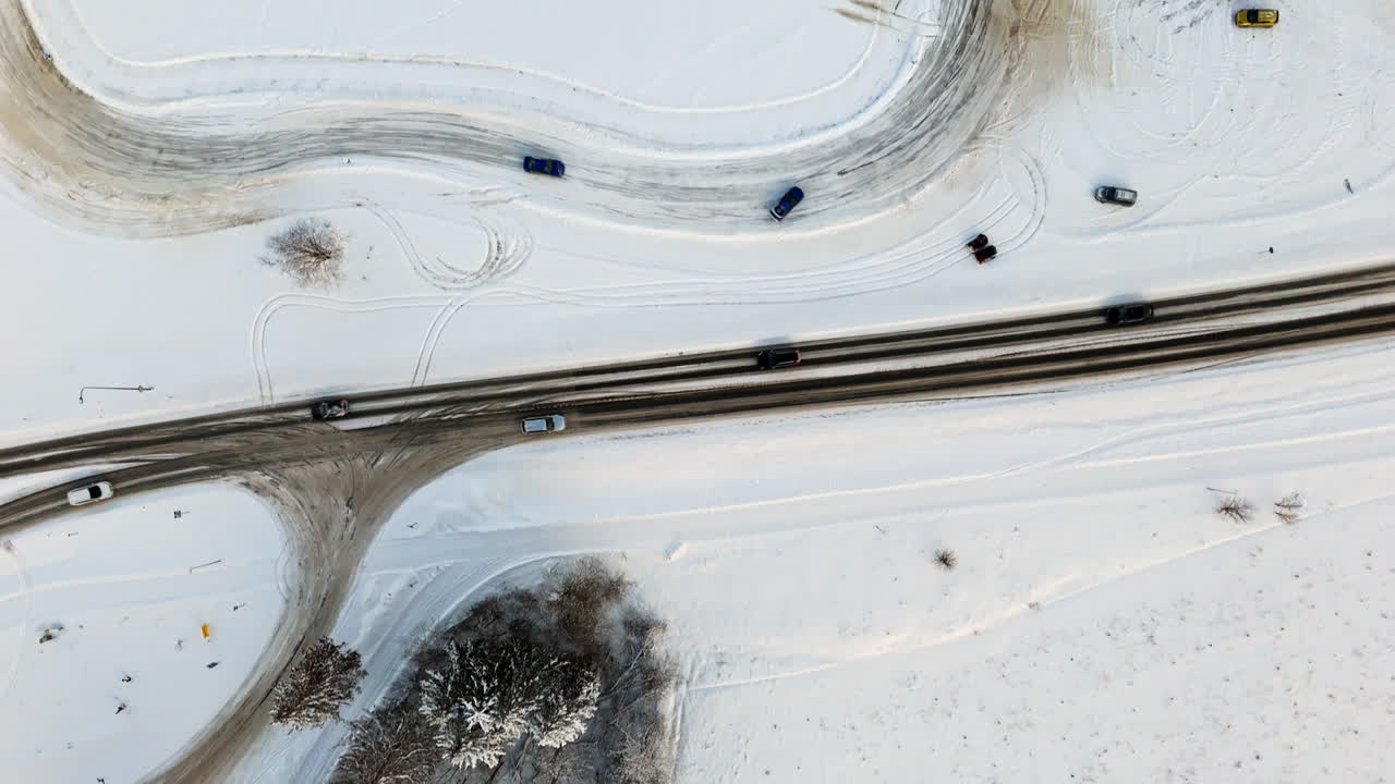 Top down drone shot over cars driving on a icy track on the snowy countryside