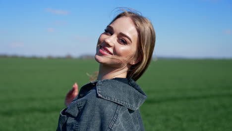attractive girl posing on camera outdoors. portrait of a young woman with long hair in denim jacket looking on camera on green field background.