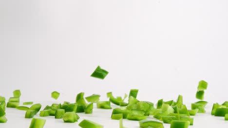 cubed green bell pepper pieces falling onto white table top and bouncing into a pile in slow motion