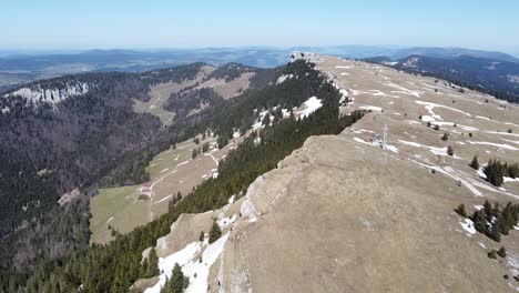 Drone-view-over-a-mountain-edge-with-thick-forest-and-lush-green-meadow,-in-the-well-known-Chasseron-in-Switzerland