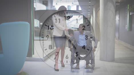 animation of ticking clock against diverse businessman on wheelchair discussing with woman at office