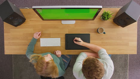 Overhead-View-Of-Male-And-Female-Graphic-Designers-Working-At-Computer-With-Green-Screen-In-Office