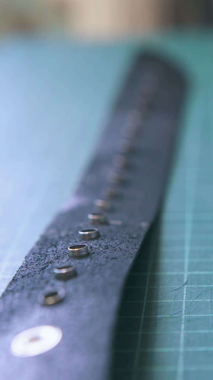 CU: Fashionable black leather belt with silver eyelets lies on green cushion board in workshop close view