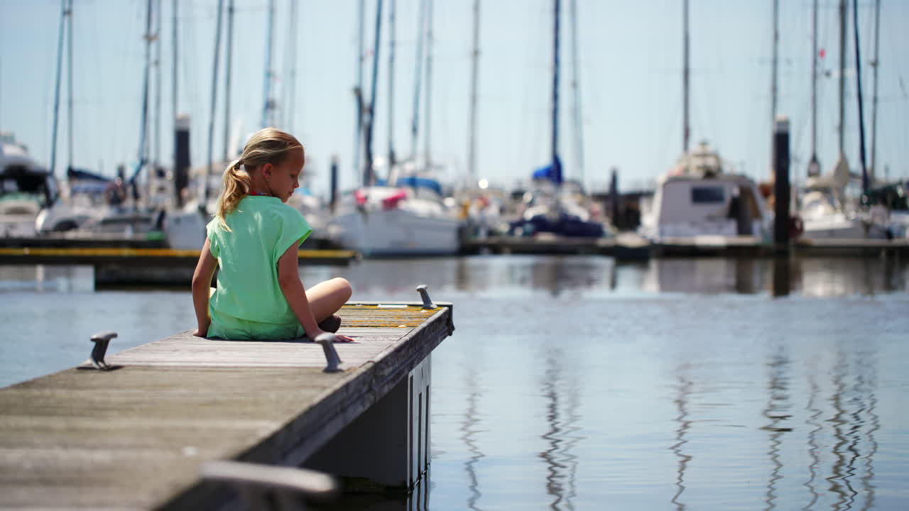 Junges Mädchen sitzt auf einem Steg und berührt das Wasser im Yachthafen.
