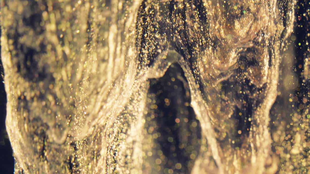 황금 잉크 입자는 검은 바탕에 다채로운 혼란으로 물에 흐른다.