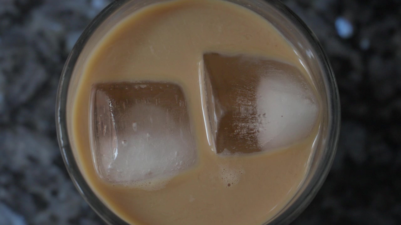 Primer plano cenital de café helado cremoso con grandes cubitos de hielo en un vaso.