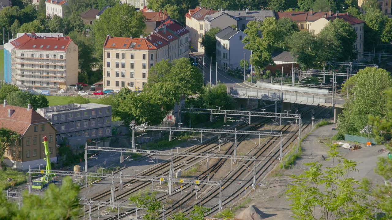 A vibrant urban area featuring colorful houses, railway tracks, and a tram passing over a bridge from left to right.