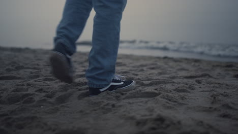 guy legs in fashionable sneakers walking on beach. man feet exploring sea coast