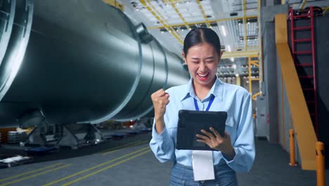 happy asian business woman celebrating using tablet in pipe manufacturing factory