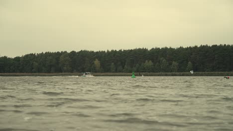 boat drives over river and hydro foil surfer try to catch the waves with forrest on coastline in slow motion