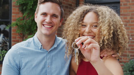 portrait of excited young couple standing outside new home holding keys together