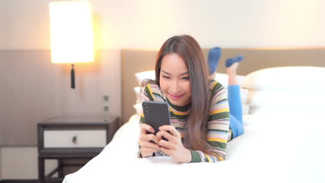 Young-Beautiful-Asian-Woman-Laying-on-Bed,-Reading-Messages,-Articles-on-Mobile-Phone