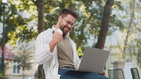 overjoyed happy young man working on laptop netbook screaming in delight in urban city street