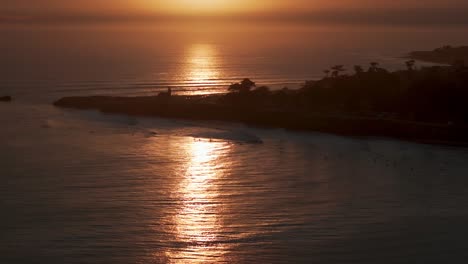 Wellen-Im-Späten-Sonnenuntergang-Brechen-Gegen-Die-Felsen-Und-Surfer-Warten-Im-Meer