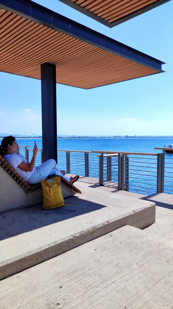 Woman relaxing on a wooden sun lounger using smartphone