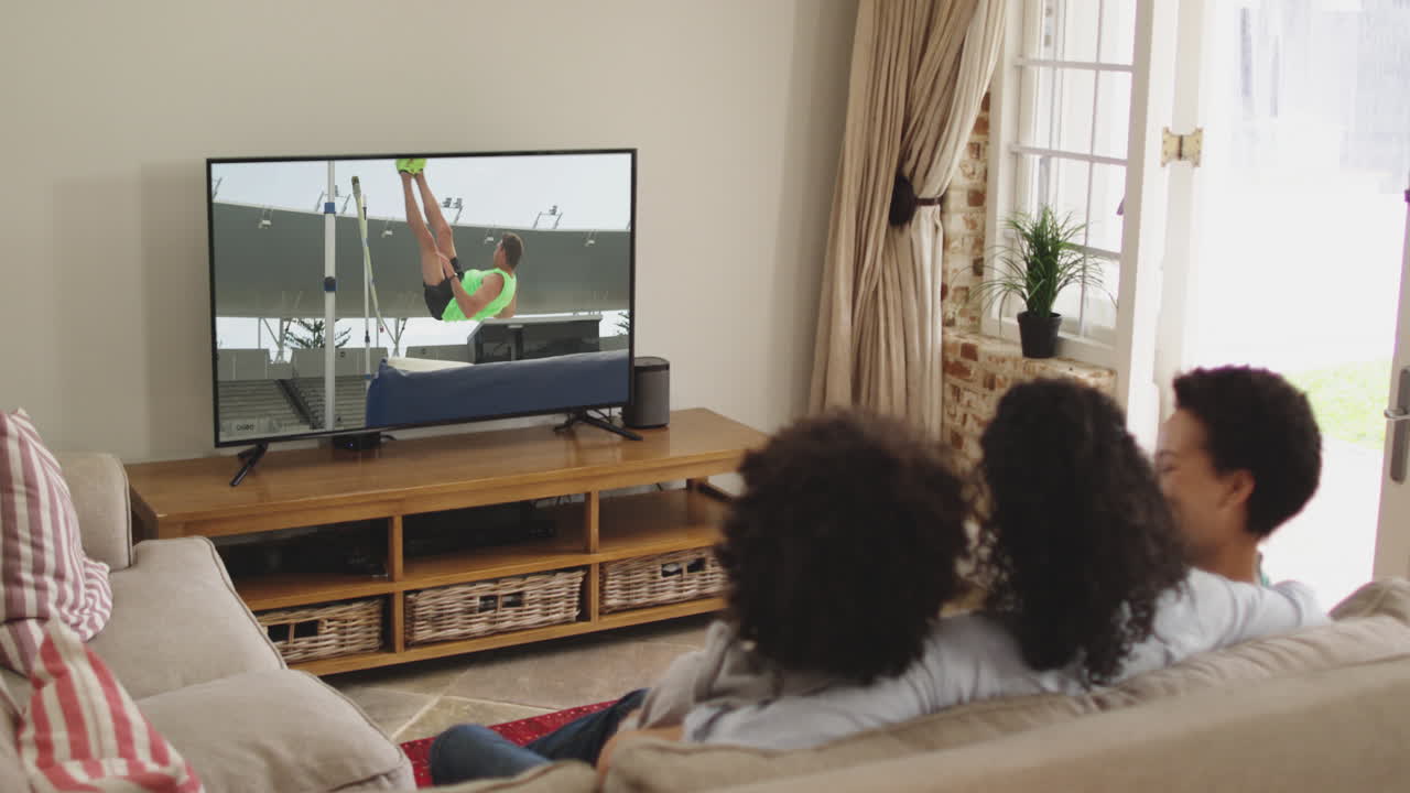 Famiglia felice seduta a casa insieme che guarda l'atletica salto in alto in TV