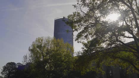 Dolly-shot-revealing-the-KolnTriangle-viewing-platform-from-behind-a-tree-backlit-by-the-sun-one-a-warm-day-and-clear-sky