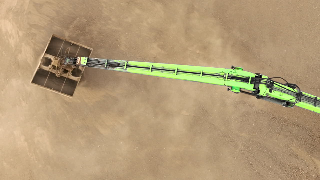 vista aérea de una grúa de construcción verde que mueve el suelo en un sitio de construcción, creando una nube de polvo