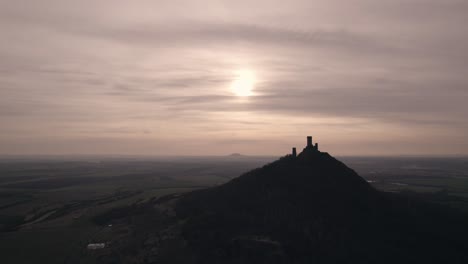 silhouette of medieval castle on hilltop with sunsetting on horizon, drone shot