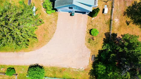 real estate aerial drone clip of a charming suburban cottage home with a generous back porch, tasteful patio furniture, and a surrounding of lush green trees creating a peaceful, inviting atmosphere