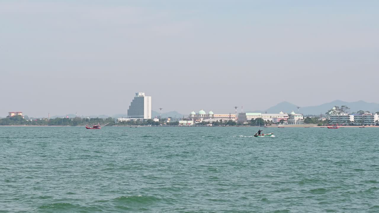 오른쪽으로 가는 작은 녹색 어선과 근처에 정박한 일부, 태국 촌부리에 있는 파타야 시를 배경으로