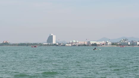 un pequeño barco de pesca verde que va a la derecha y algunos anclados cerca y la ciudad de pattaya en el fondo en chonburi, tailandia