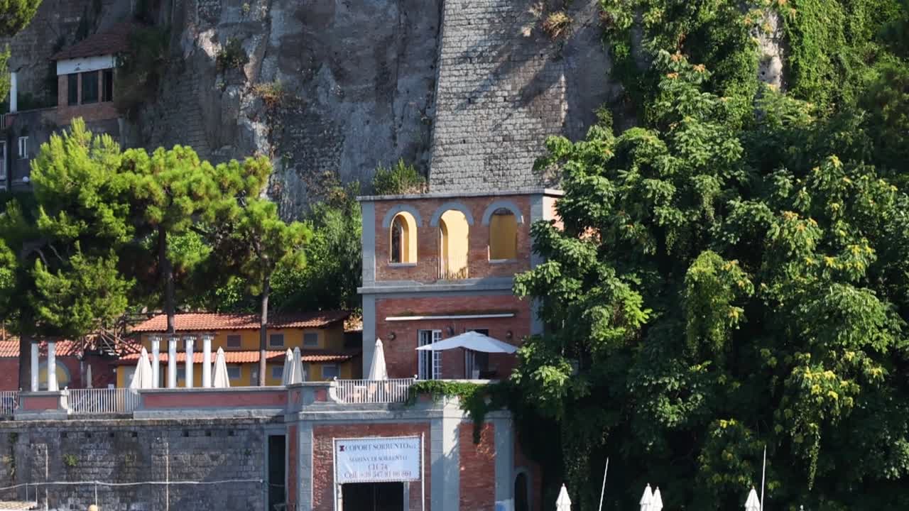 Barche solcano le acque blu del Mediterraneo ai piedi di ripide scogliere e di un grandioso hotel sul lungomare